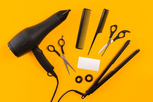 Black hair dryer, comb and scissors on yellow paper background. Top view photo