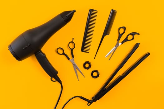 Black hair dryer, comb and scissors on yellow paper background. Top view photo