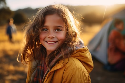 Portrait of cute little girl at camera while standing near camping tent at sunset AI generated photo