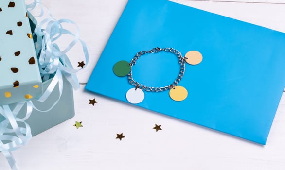Shiny silver or platinum bracelet on blue cardboard next to a gift box isolated on white background. Close up, copy space photo
