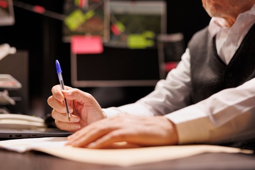 Senior police officer writing missing person case report, working overhours at criminal case in arhive room. Old investigator analyzing criminology files, planning startegy to catch suspect. Close up photo