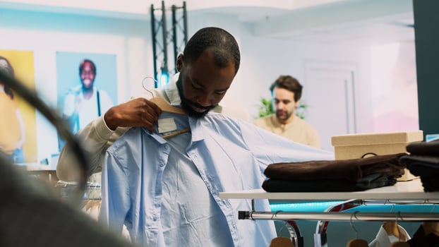 Male retail customer picking up clothes from racks, looking at department store merchandise to buy on discount. Young adult visiting shopping mall as client, commercial activity. Handheld shot. photo