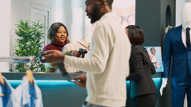 Asian client preparing to pay for clothes at cash register, talking to store assistant before buying modern merchandise. Young customer making purchase at pos terminal in clothing store. photo