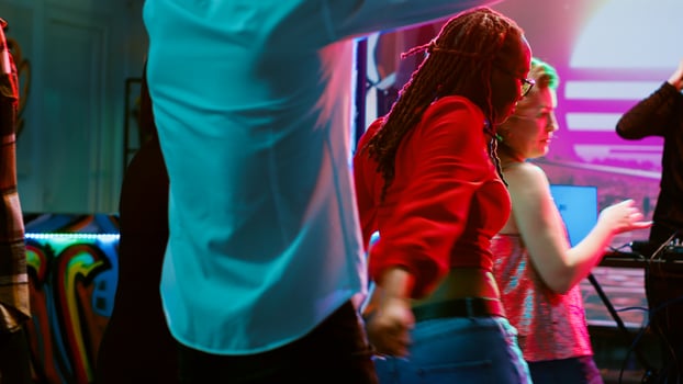 Multiethnic group of people dancing in discotheque, having fun together with electronic music on dance floor. Crowd of friends jumping and partying at nightclub, disco spotlights. photo