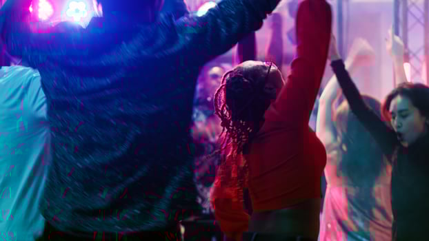 Cheerful persons jumping at nightclub, having fun partying on electronic mixing music at modern party. Cool people enjoying night out on club dance floor, live show performance. Tripod shot. photo