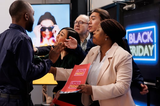 Frenzy diverse people shoppers standing at store entrance going crazy for Black Friday deals. African American man security officer managing crowd control during seasonal sales photo