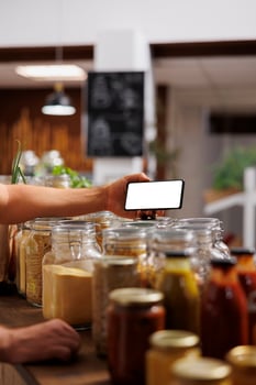 Client in zero waste shop using mockup mobile phone to analyze pantry staples. Vegan customer thoroughly checking local supermarket food items are allergens free with isolated screen smartphone photo