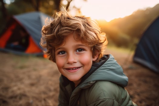 Portrait of a cute boy looking at camera while near his tent in nature AI generated photo