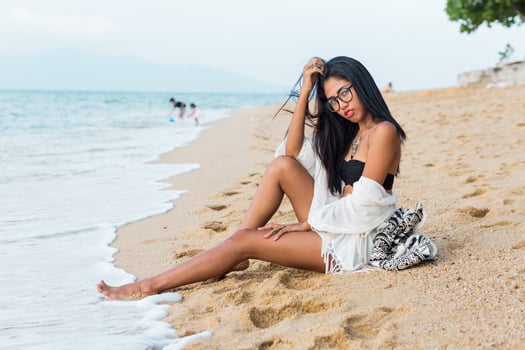 Asian woman with red lips posing on tropical beach in the evening. Wearing boho white cover up, back pack with stylish print. Perfect tan body. Stylish Sumer outfit.Jewelry ,bracelet and necklace. photo