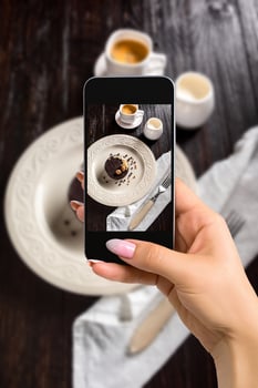 Photographing food concept - woman takes picture of beautiful decorated chocolate cake with golden nuts and a cup of coffee photo