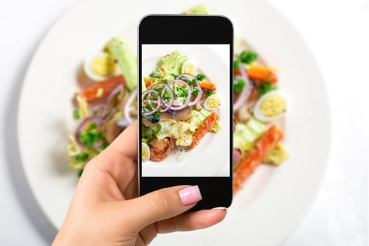 Photographing food concept - woman takes picture of fresh salad with lettuce, eggs, tomatoes, onion rings, peppers photo