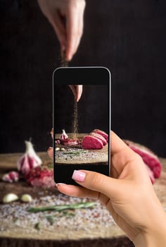Photographing food concept - woman takes picture of juicy raw beef steak on wooden table photo