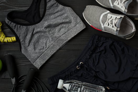 Athlete's set with female clothing, sneakers and bottle of water on dark background photo