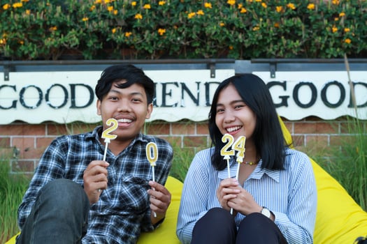 happy couple teen multi racial holding number 20 24 candle and sitting on the yellow bean bag in house yard grass with flower background, look to camera photo