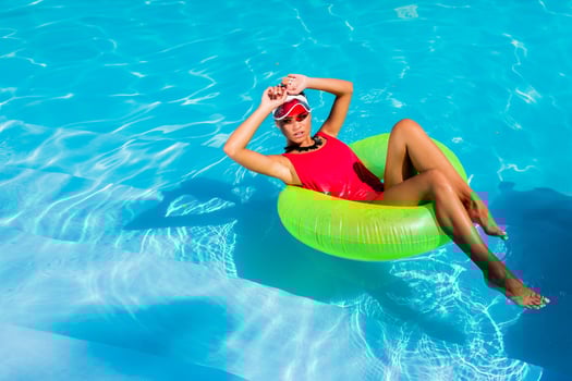 Sexy tanned    woman in red swimsuit having fun and enjoying  summer in amazing big swimming pool. Young pretty girl  swimming on inflatable ring.  Stylish transparent cap. Beach party. photo