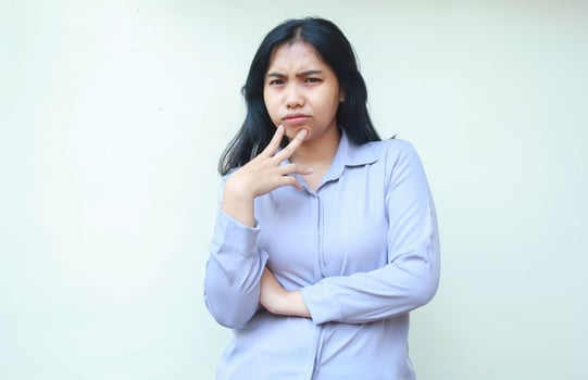 thoughful serious asian young woman employee looking to camera suspiciously with folded arm and touching chin isolated on white background photo