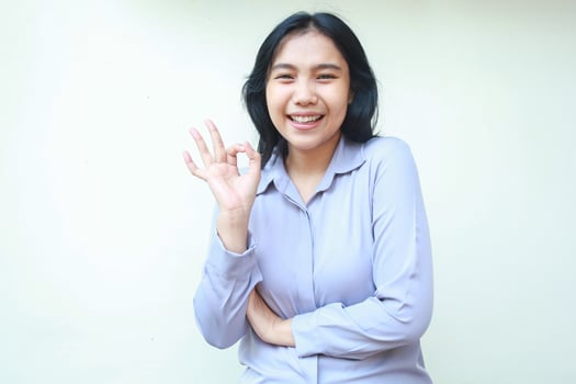 beautiful asian young business woman dressed in formal shirt posing ok sign with folded arm looking to camera smiling satisfied, approve symbol gesture of female worker isolated in white background photo