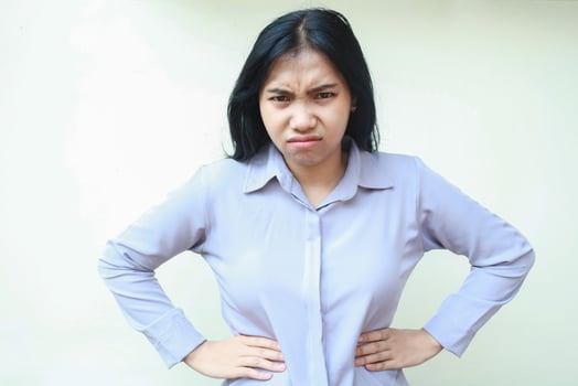 portrait of upset dissappointed asian young business woman looking to camera with angry face expression and hand on waist wearing formal suit isolated over white background photo