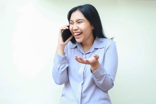 studio shot of laughing asian young business woman speaking on cellphone smiling broadly looking away wear purple formal office shirt standing over isolated white background photo