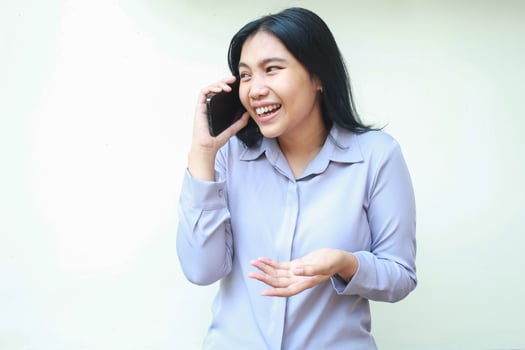 image of happy asian young business woman enjoy speaking on moblie phone with rejoicing laugh dressed in fromal purple shirt looking away standing over isolated white background photo