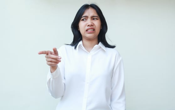 image of displeased asian woman boss pointing beside and looking away with disgusted face expression wearing white formal shirt standing over isolated background photo
