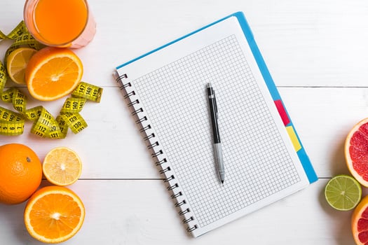 Fresh juice in glass from citrus fruits - lemon, grapefruit, orange, notebook with pencil on white wooden background photo