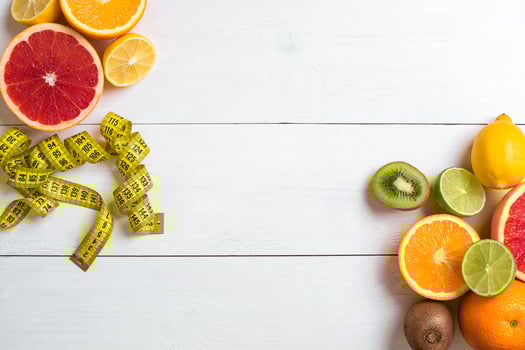 Fresh fruits with tape measure over white wooden background. Top view photo