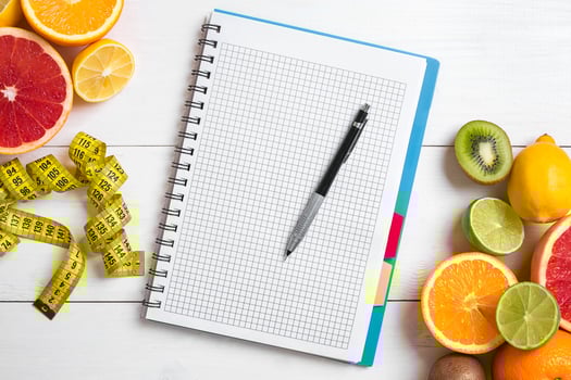 Fresh juice in glass from citrus fruits - lemon, grapefruit, orange, notebook with pencil on white wooden background photo