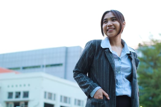 portrait of confident asian business woman standing in outdoors city street wearing formal grey jacket and blue stripe shirt with urban bulding background, female financial manager walking in outside photo