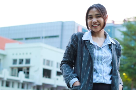 portrait of confident asian business woman standing in outdoors city street wearing formal grey jacket and blue stripe shirt with urban bulding background, female financial manager walking in outside photo