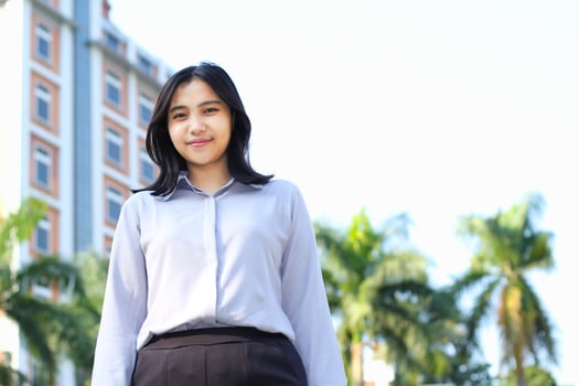 low angle view of asian businesswoman consultant manager wearing formal suit smiling at camera standing over city building and green plant background photo