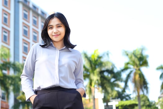 low angle view of asian businesswoman consultant manager wearing formal suit smiling at camera standing over city building and green plant background photo
