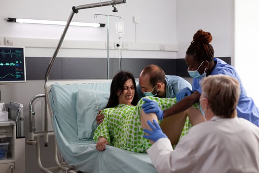 Diverse obstetrician doctor helping woman to delivery baby, being comforting by husband in hospital ward. Pregnant patient with painful labor contractions pushing while giving birth to child photo