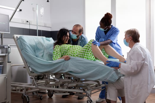 Woman pushing to give birth to baby in hospital ward, having painful contractions during caesarean surgery. Obstetrician doctor and husband comforting pregnant patient in maternity clinic photo