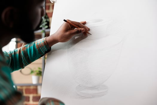 Student guy drawing with pencil on canvas. African American man artist staying focused while creating art in studio or workshop, sitting at easel sketching basic vase using pencil photo