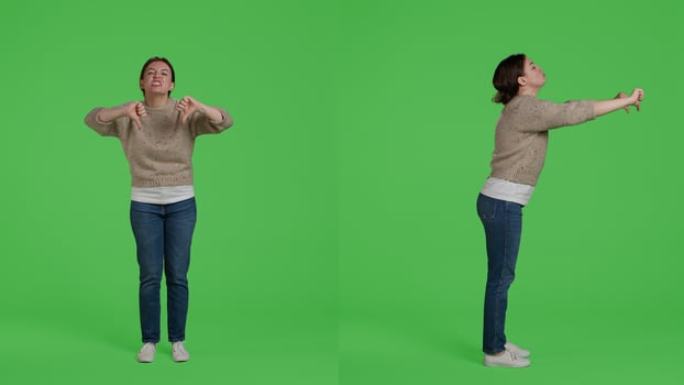 Female model showing thumbs down negative sign on camera, doing disapproval and bad symbol. Confident woman expressing disagreement with dislike gesture over full body greenscreen. photo