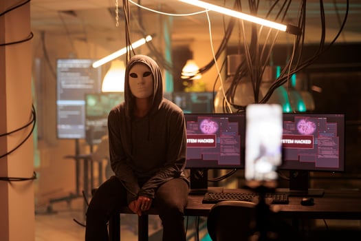 Young hacker with anonymous mask attacking computer server, committing cybercrime. Database system hacking, information phishing, system malware programming, cyber criminal working at night. photo