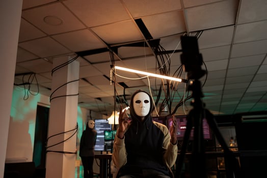Ransomware cyberattack, information leak, scammer speaking on smartphone camera, asking victim money for ransom. Man hacker in mask stealing finances online at night time, internet fraud photo