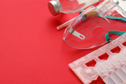Coronavirus treatment concept. A medical face mask nebulizer for treatment of respiratory tract and packs of ampoules flat layed on red background photo
