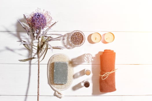 Spa set with sea salt, essential oil, soap and towel decorated with dry flower on white wooden background. Sun flare photo