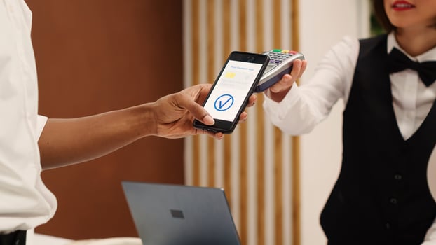 Close up of african american tourist using smartphone banking app to pay for room upgrade during check in process. Receptionist using POS payment terminal to validate credit card purchase photo