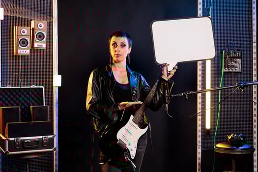Guitarist woman showing blank placard with copy space for advertisement in music studio, person playing electric guitar preparing for rock concert. Musician with leather outfit performing heavy metal photo