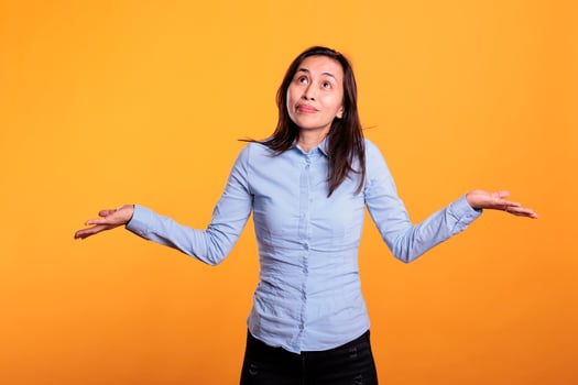 Pensive doubtful woman shrugging shoulders doing i dont know gesture, posing indecisive in studio over yellow background. Filipino young adult making confused uncertain facial expression. photo