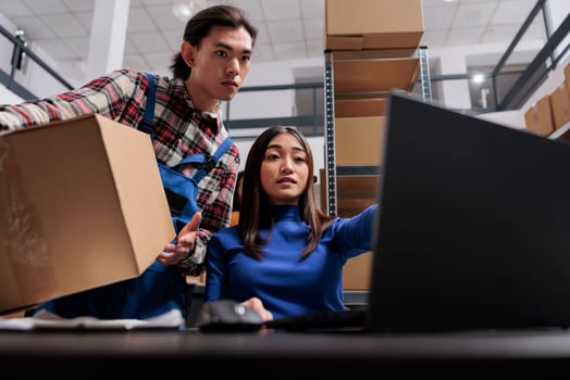 Post office warehouse asian workers preparing package for dispatching. Shipment company employees team doing inventory management using software on laptop in storage room photo