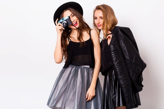 fashion portrait of two elegant stylish  women wearing a leather  skirt and black hat , holding  retro camera.  Posing against white background. photo