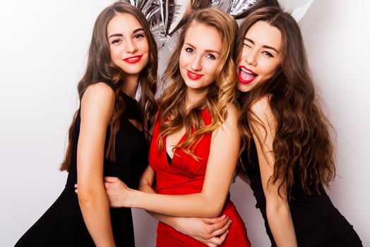 Three best friends celebrate  birthday indoor wearing elegant evening dress and have bright make up. Girls hugging and Showing signs with their hands. Looking at camera and smiling. Inside. photo
