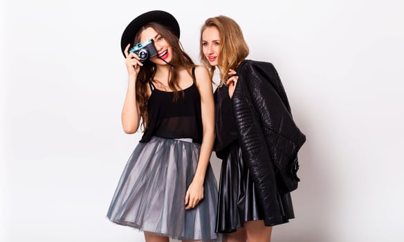 fashion portrait of two elegant stylish  women wearing a leather  skirt and black hat , holding  retro camera.  Posing against white background. photo