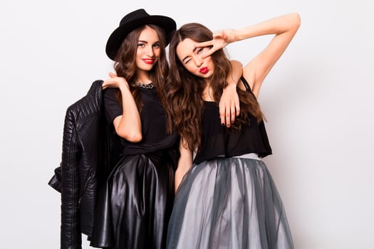 fashion portrait of two elegant stylish women wearing a leather skirt and black hat. Posing against white background.They smiling and looking at camera. photo