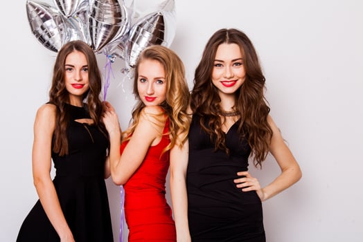 Three best friends celebrate  birthday indoor wearing elegant evening dress and have bright make up. Girls hugging and Showing signs with their hands. Looking at camera and smiling. Inside. photo
