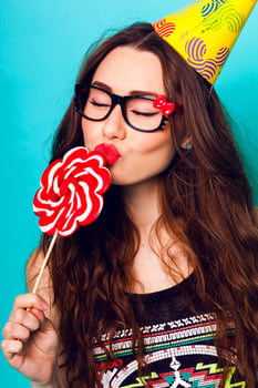 Studio closeup colorful portrait of young sexy funny fashion crazy  woman kiss big lollipop wearing summer  clothes ,  paper hat and cute glasses. photo